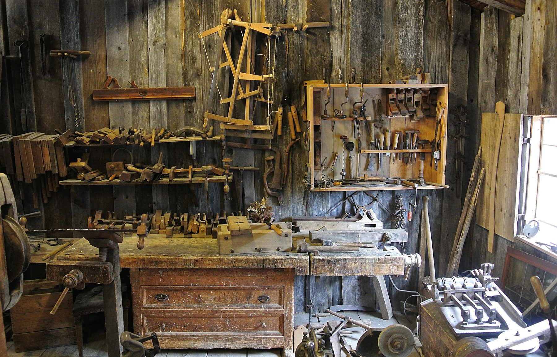 Interno di una vecchia bottega da falegname con banco da lavoro, attrezzi appesi e trucioli