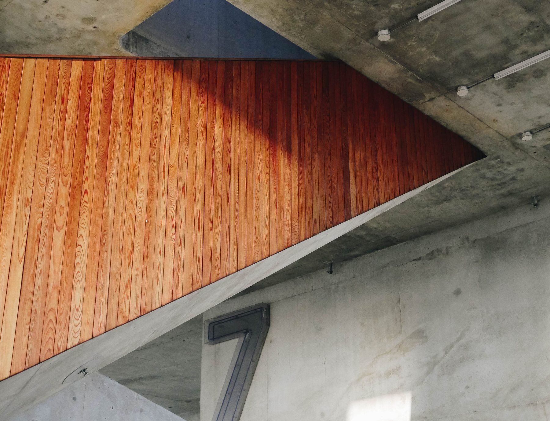 Rivestimento di doghe di legno rossiccio sotto una scala in cemento